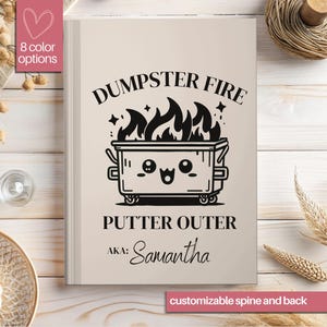 May include: A beige journal with a black and white illustration of a dumpster fire with a cute face. The text "DUMPSTER FIRE" is above the illustration and "PUTTER OUTER" is below the illustration. The text "AKA: Samantha" is below the text "PUTTER OUTER".