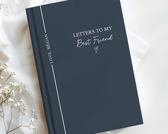 May include: A navy blue journal with the text "Letters to My Best Friend" in white script. A white vertical line runs down the left side, with "Love, Megan" printed vertically. The journal is on a white surface.