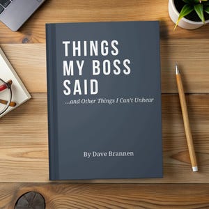 May include: A book titled "THINGS MY BOSS SAID...and Other Things I Can't Unhear" by Dave Brannen. The book has a dark blue cover with white text. The book is on a wooden surface with a pencil, glasses, and a laptop.