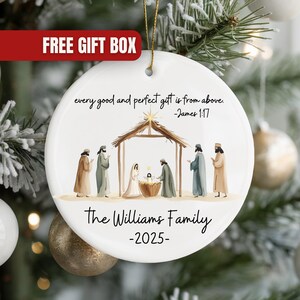 May include: A white ceramic Christmas ornament with a Nativity scene illustration. The ornament features the text "every good and perfect gift is from above - James 1:17" and "The Williams Family -2025-". A red banner with "FREE GIFT BOX" is at the top.
