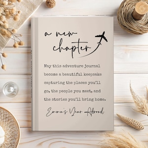 May include: A beige journal with the words "a new chapter" and a small airplane illustration. The text below reads "May this adventure journal become a beautiful keepsake capturing the places you'll go..." and "Emma's Year Abroad."
