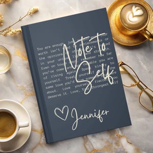 May include: A dark blue journal with the text "Note to Self" in white lettering. The journal has a white heart and the name "Jennifer" written in cursive.