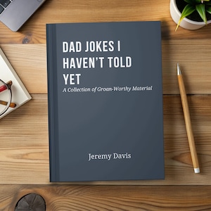May include: A hardcover book titled "DAD JOKES I HAVEN'T TOLD YET" with the subtitle "A Collection of Groan-Worthy Material" by Jeremy Davis. The book has a dark blue cover and is on a wooden surface.