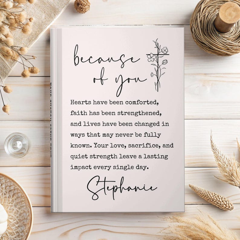 May include: A hardcover book with the text "because of you" in elegant script. The book's pages display a message about faith and love, with the name "Stephanie" at the bottom. A cross and floral design is on the right side.