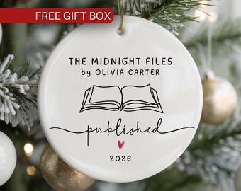 May include: A round white ceramic ornament featuring the black text THE MIDNIGHT FILES by OLIVIA CARTER, a line art illustration of an open book, the word published in script, a small red heart, and the year 2026, hanging by a gold string.