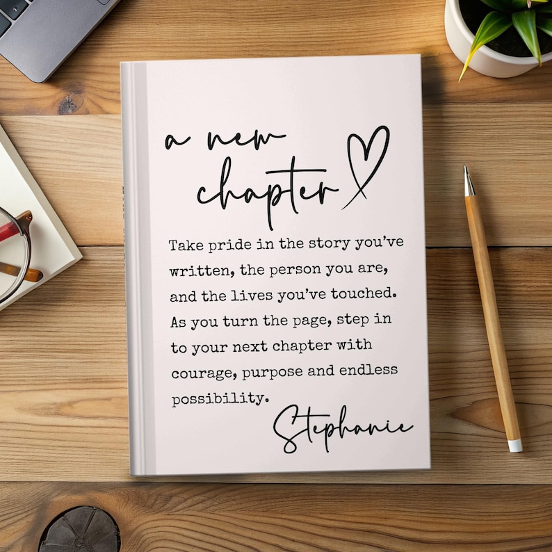 May include: A white journal with the words "a new chapter" and a heart symbol in black script. The text below reads, "Take pride in the story you've written..." and is signed "Stephanie". A pencil and plant are on a wooden surface.