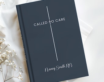 May include: A navy blue journal with the text "CALLED TO CARE" and "Nancy Smith, RN" in white script. A vertical white line intersects the text. The journal is on a white surface with delicate white flowers.