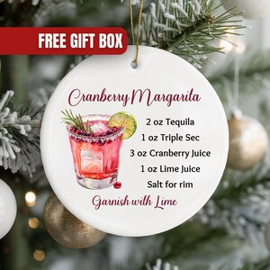 May include: White ceramic Christmas ornament with a cranberry margarita recipe. The ornament features a watercolor illustration of the cocktail, with ingredients listed: 2 oz tequila, 1 oz triple sec, 3 oz cranberry juice, 1 oz lime juice, and salt for the rim.