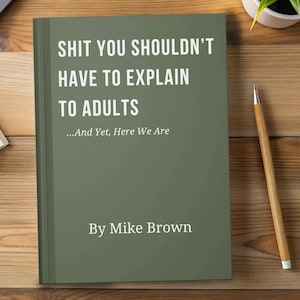 May include: A book with a matte olive green cover featuring white text that reads: SHIT YOU SHOULDN'T HAVE TO EXPLAIN TO ADULTS ...And Yet, Here We Are By Mike Brown. The book is positioned vertically on a wooden surface next to a wooden pencil.
