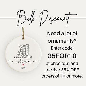 May include: A round white ceramic ornament with a gold hanging string. The design features a black line drawing of four books, the text "WILLOW BOOK CLUB", the name "olivia", a small red heart, and the year "2026". Text reads "Bulk Discount".