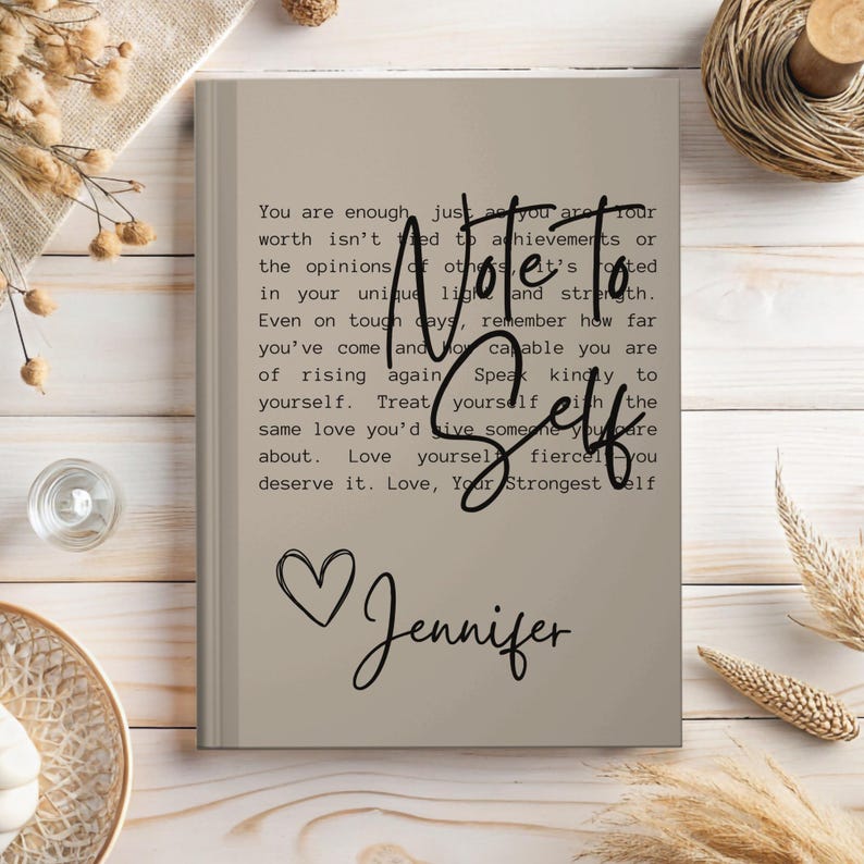 May include: A beige journal with a motivational quote about self-love and a heart with the name Jennifer written in cursive.