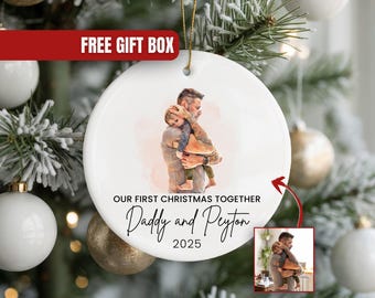 May include: White ceramic Christmas ornament with a watercolor image of a father holding a child. Text reads "OUR FIRST CHRISTMAS TOGETHER Daddy and Peyton 2025". Includes a small inset image. A red banner says "FREE GIFT BOX".