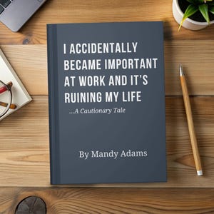 May include: A hardback book with a dark blue cover, titled "I Accidentally Became Important at Work and It's Ruining My Life" by Mandy Adams. The book is on a wooden desk with a pencil and a small plant.