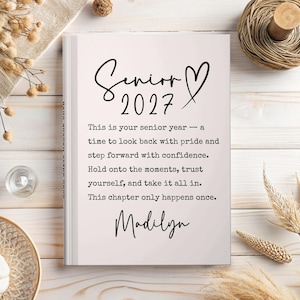 Op de afbeelding: Een hardcover boek met de tekst "Senior 2027" in een scriptlettertype, met een hartsymbool. De pagina's van het boek zijn lichtroze en de tekst bevat inspirerende citaten en de naam "Madilyn".