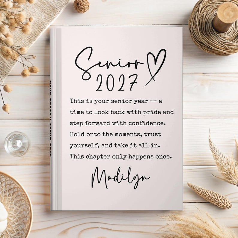 Op de afbeelding: Een hardcover boek met de tekst "Senior 2027" in een scriptlettertype, met een hartsymbool. De pagina's van het boek zijn lichtroze en de tekst bevat inspirerende citaten en de naam "Madilyn".