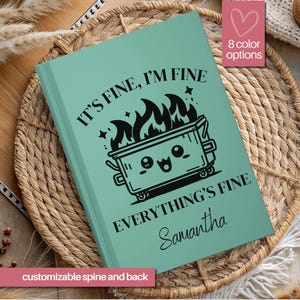 May include: A teal green journal with a black and white illustration of a trash can with flames and the text "It's fine, I'm fine, Everything's fine, Samantha".