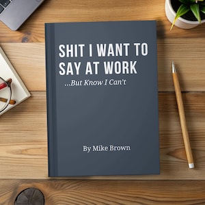 May include: A dark gray hardcover book with white text that reads SHIT I WANT TO SAY AT WORK ...But Know I Can't By Mike Brown. The book is positioned on a wooden surface next to a wooden pencil, a pair of glasses, and a small potted plant.