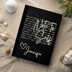 May include: Black journal with a white heart and the text "Note to Self" and "You are enough just as you are. Your worth isn't tied to achievements or the opinions of others. Remember how far you've come and how capable you are. Speak kindly to yourself. Treat yourself with the same love you'd give someone you care about. Love yourself fiercely. Love, Your Strongest Self" and the name "Jennifer" written in cursive.
