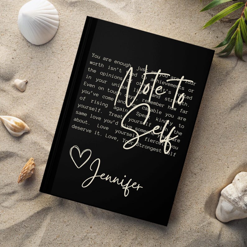 May include: Black journal with a white heart and the text "Note to Self" and "You are enough just as you are. Your worth isn't tied to achievements or the opinions of others. Remember how far you've come and how capable you are. Speak kindly to yourself. Treat yourself with the same love you'd give someone you care about. Love yourself fiercely. Love, Your Strongest Self" and the name "Jennifer" written in cursive.