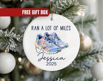 May include: White ceramic Christmas ornament with a watercolor image of running shoes. The text "RAN A LOT OF MILES" is above the shoes, with "Jessica" and "2025" below. The ornament hangs on a Christmas tree.