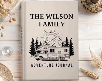 May include: A beige hardcover journal with black text reading THE WILSON FAMILY ADVENTURE JOURNAL. The cover features a black graphic illustration of a motorhome parked in front of a mountain range, a sunburst, and pine trees.