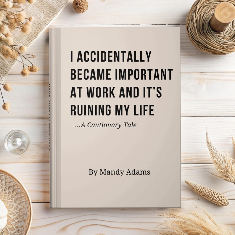 May include: A hardback book with a light beige cover featuring the black text: I ACCIDENTALLY BECAME IMPORTANT AT WORK AND IT'S RUINING MY LIFE ...A Cautionary Tale By Mandy Adams. The book is positioned centrally on a light wooden surface.