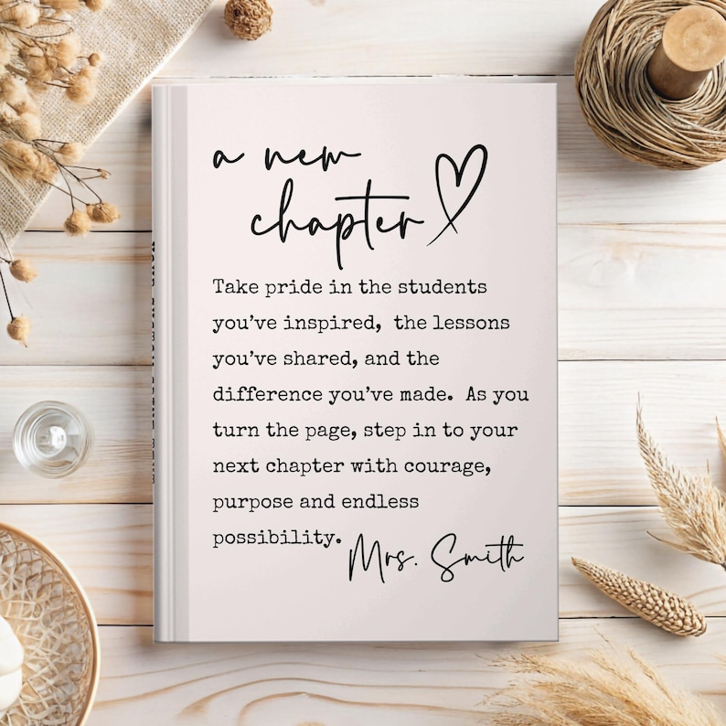 Puede incluir: Un libro blanco con las palabras "a new chapter" y un s&iacute;mbolo de coraz&oacute;n. El texto de abajo dice: "Take pride in the students you've inspired..." y est&aacute; firmado "Mrs. Smith". El libro est&aacute; sobre una superficie de madera clara.