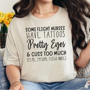 May include: A white t-shirt with black text that reads "Some flight nurses have tattoos, pretty eyes & cuss too much. It's me, I'm some flight nurses."