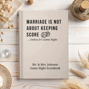 May include: A beige scorebook with black text that reads Marriage Is Not About Keeping Score...Unless It's Game Night, followed by Mr. & Mrs. Johnson Game Night Scorebook. The cover features a graphic of two dice in the center of the text.