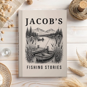 May include: A hardcover book with a light beige cover featuring the black text JACOB'S FISHING STORIES. The cover illustration depicts a black and white line drawing of a wooden rowboat docked at a pier, surrounded by cattails, with a lake, forest, and mountains in the background.