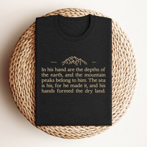 Könnte beinhalten: Schwarzes T-Shirt mit einem goldenen Bergmotiv und dem Text "PSALM 95:4 In seiner Hand sind die Tiefen der Erde, und die Gipfel der Berge gehören ihm. Das Meer gehört ihm, denn er hat es gemacht, und seine Hände haben das trockene Land geformt."