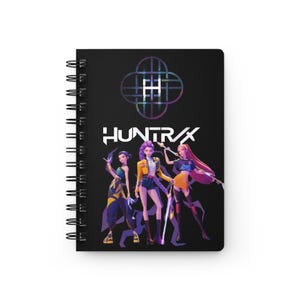 May include: Spiral-bound notebook with a black cover featuring the text "HUNTRAX" in white and a colorful graphic. The cover art depicts three stylized female figures in dynamic poses, with a geometric logo above the text.