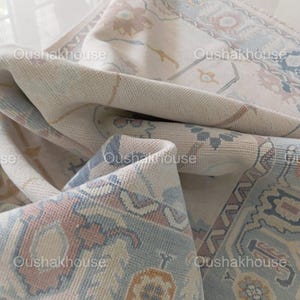 May include: A close-up of a cream-coloured rug with a blue and pink floral pattern. The rug is folded in half, revealing the underside of the rug.
