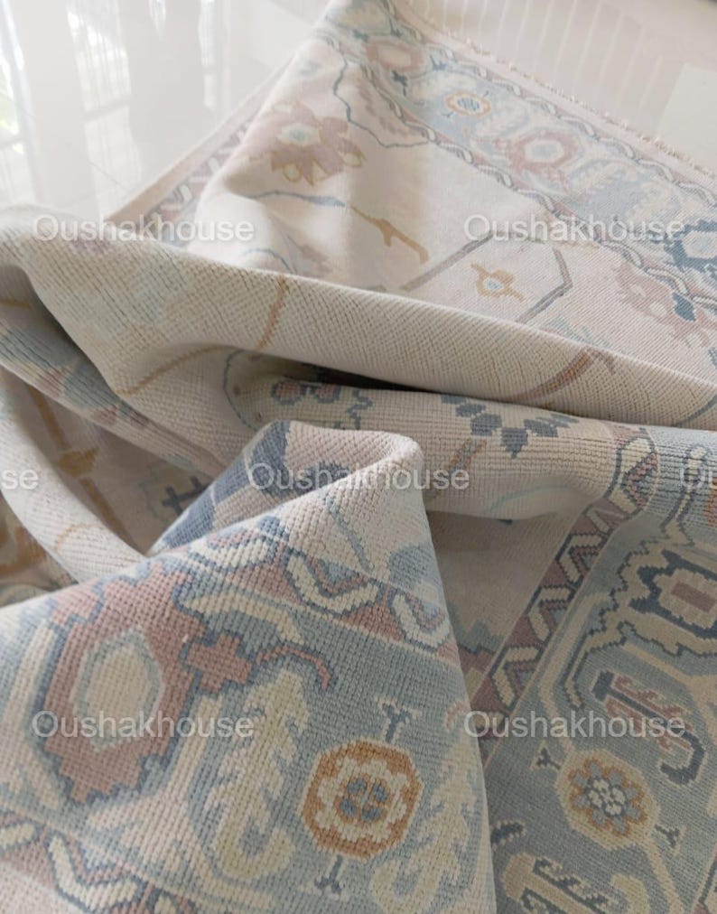 May include: A close-up of a cream-coloured rug with a blue and pink floral pattern. The rug is folded in half, revealing the underside of the rug.