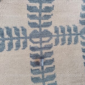 Op de afbeelding: Een kleine, zilverkleurige metalen steeksleutel met de tekst "SKA" erop gedrukt. De sleutel ligt op een beige en blauw gepatroneerd tapijt.