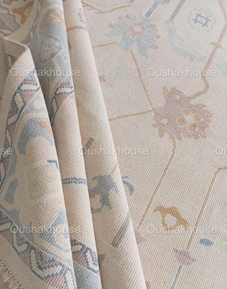 May include: A beige rug with a light blue and pink floral pattern. The rug is folded in thirds, showing the pattern on the front and back sides.