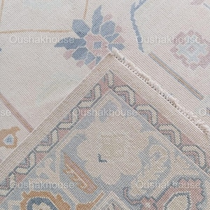 May include: Close-up of a cream-coloured rug with a detailed floral pattern in shades of blue, pink, and brown. The rug has a fringed edge.