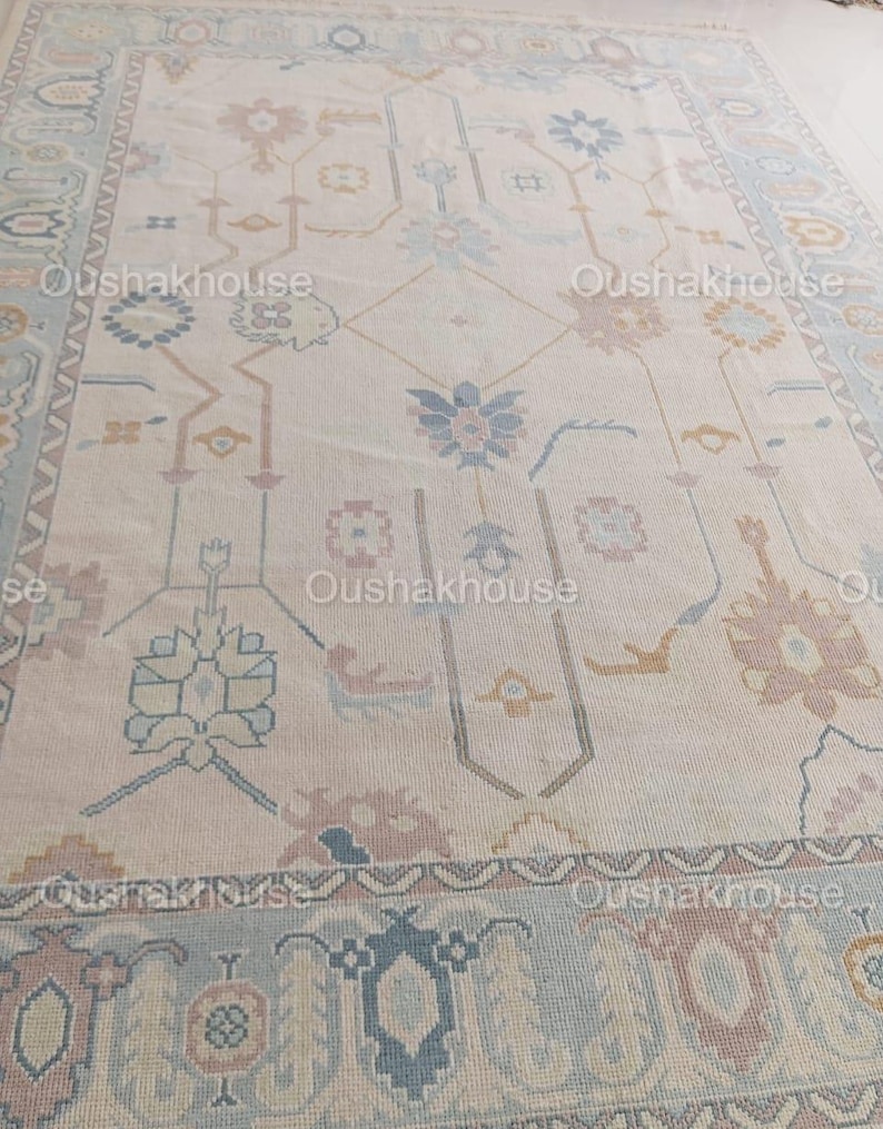 May include: A cream-coloured rug with a traditional Persian design featuring intricate floral patterns in shades of blue, pink, and beige. The rug has a border with a repeating geometric pattern.