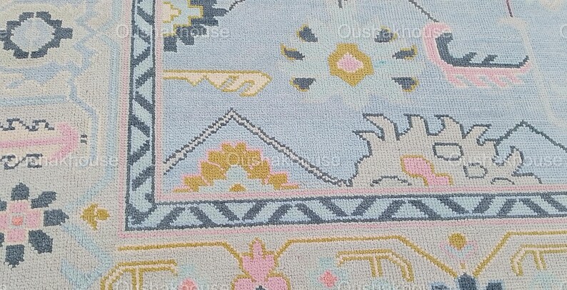 May include: A close-up of a light blue rug with a geometric pattern in shades of pink, yellow, and blue. The rug has a border with a zig-zag pattern.