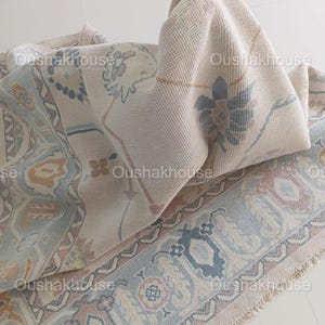 May include: A cream-coloured rug with a blue and pink floral pattern. The rug has a fringe border and is folded in half.