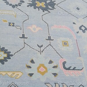 May include: A light blue rug with a geometric pattern in shades of pink, yellow, and gray. The rug has a border with a repeating pattern.