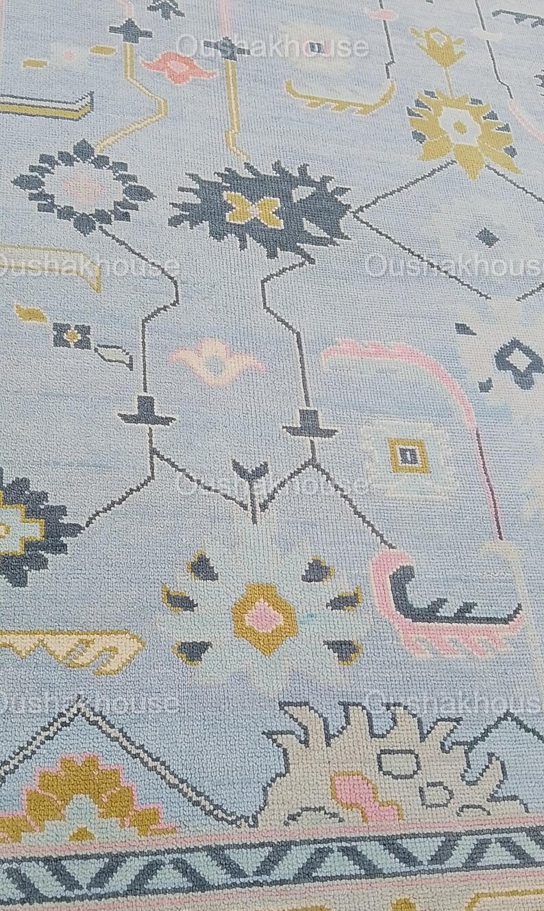 May include: A light blue rug with a geometric pattern in shades of pink, yellow, and gray. The rug has a border with a repeating pattern.