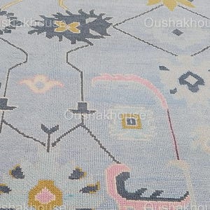 May include: A light blue rug with a geometric pattern in shades of pink, yellow, and gray. The pattern features stylized flowers and leaves.