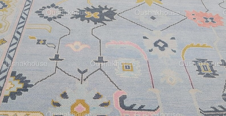 May include: A light blue rug with a geometric pattern in shades of pink, yellow, and gray. The pattern features stylized flowers and leaves.