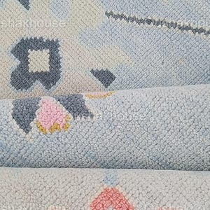 May include: Close-up of a blue, pink, and yellow patterned rug with a soft, textured surface.