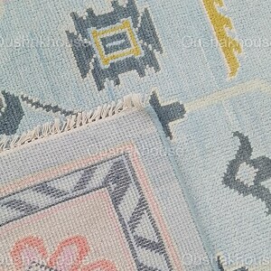 May include: Close-up of a blue and pink patterned rug with a fringe border. The rug has a geometric design with a central flower motif.
