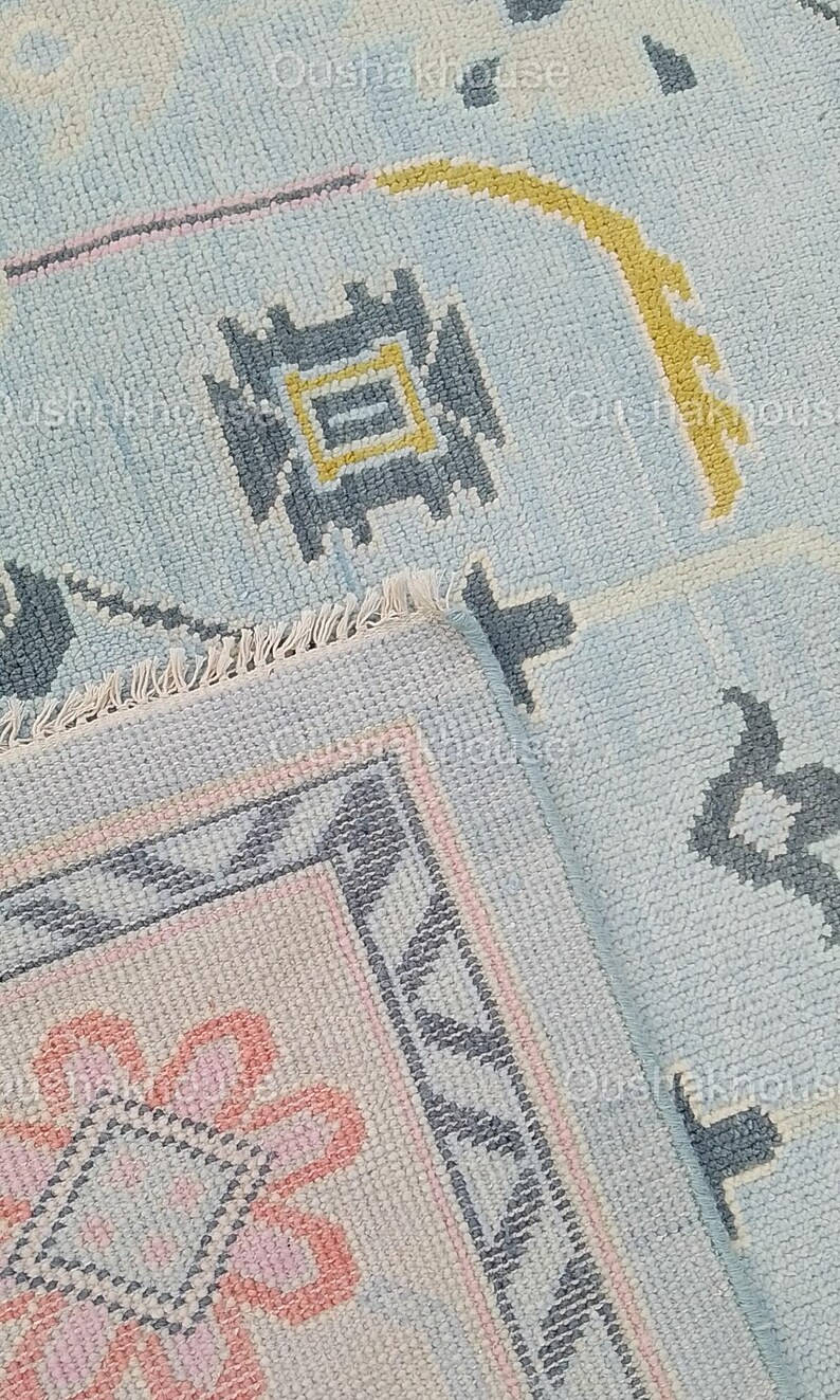 May include: Close-up of a blue and pink patterned rug with a fringe border. The rug has a geometric design with a central flower motif.