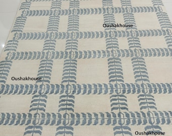Könnte beinhalten: Rechteckiger, cremefarbener Teppich mit einem Gittermuster aus blauen, blattartigen Designs. Der Teppich hat einen Fransenrand und der Text "Oushakhouse" ist sichtbar. Geeignet für Wohnzimmer, Schlafzimmer oder Eingangsbereiche.