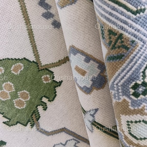 May include: Close-up of a white rug with a green, blue, and brown floral pattern. The rug is folded in thirds, showing the pattern from different angles.