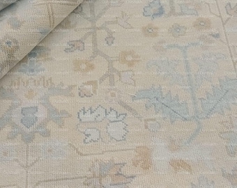 May include: A rolled-up area rug with a cream-colored background and a detailed floral pattern in shades of blue and tan. The rug's design features intricate floral motifs and a textured surface, showcasing a classic, elegant style.